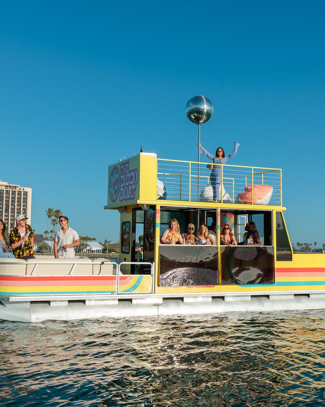 The Disco Boat at sunset — rooftop disco ball lit up, guest waving from the upper deck